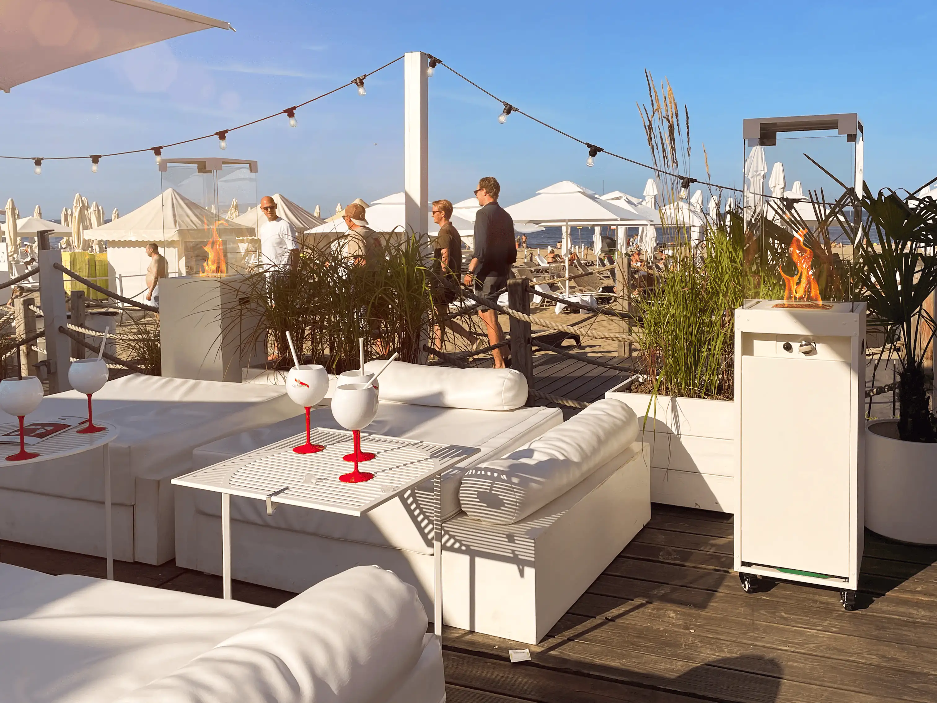 Ein Außenkamin steht neben weißen Sofas in einer Strandbar